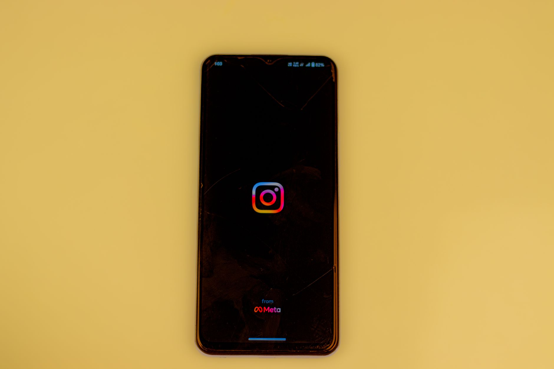 A smartphone displays the Instagram app opening screen against a vibrant yellow background.