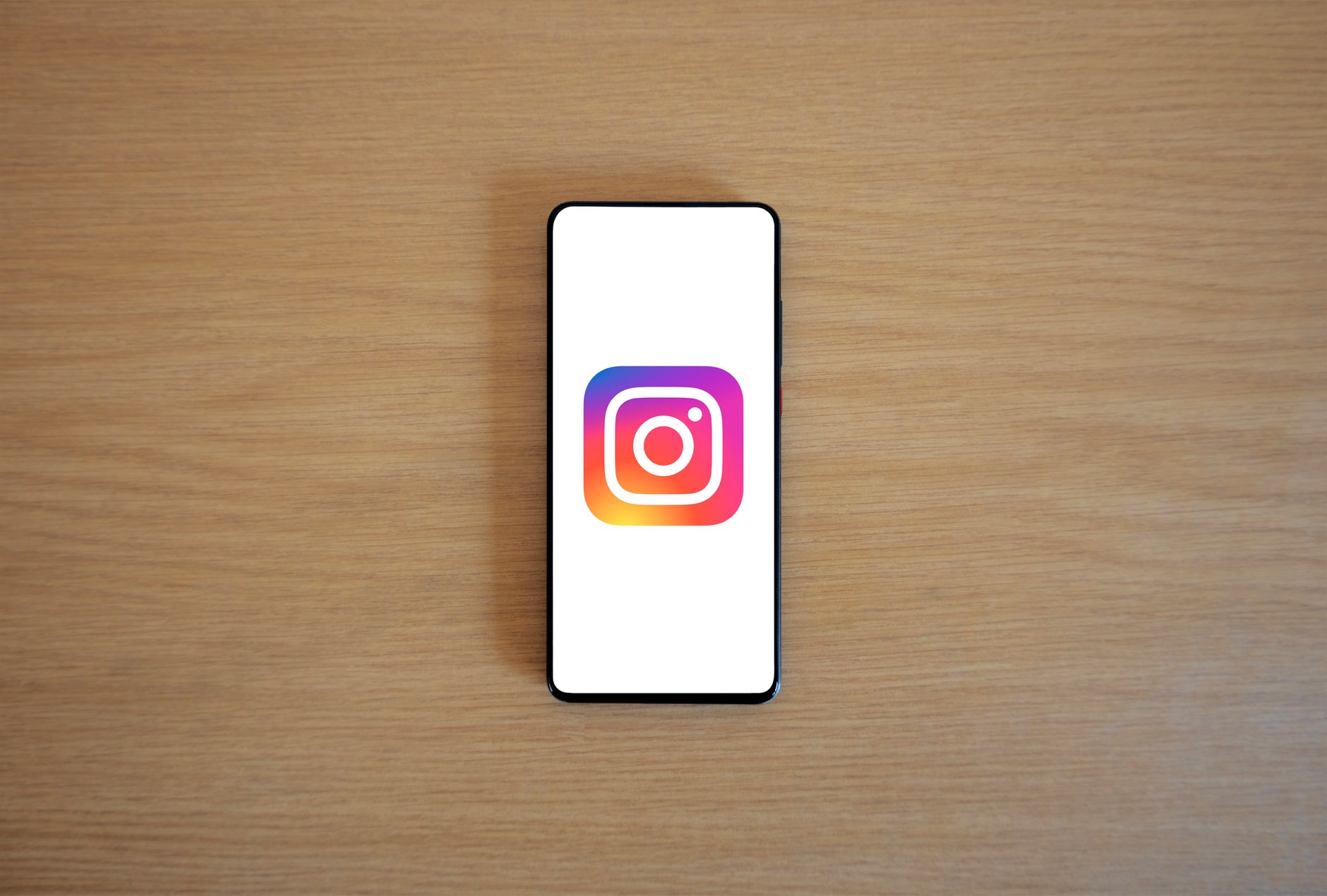 Instagram app icon displayed on a smartphone screen resting on a wooden desk