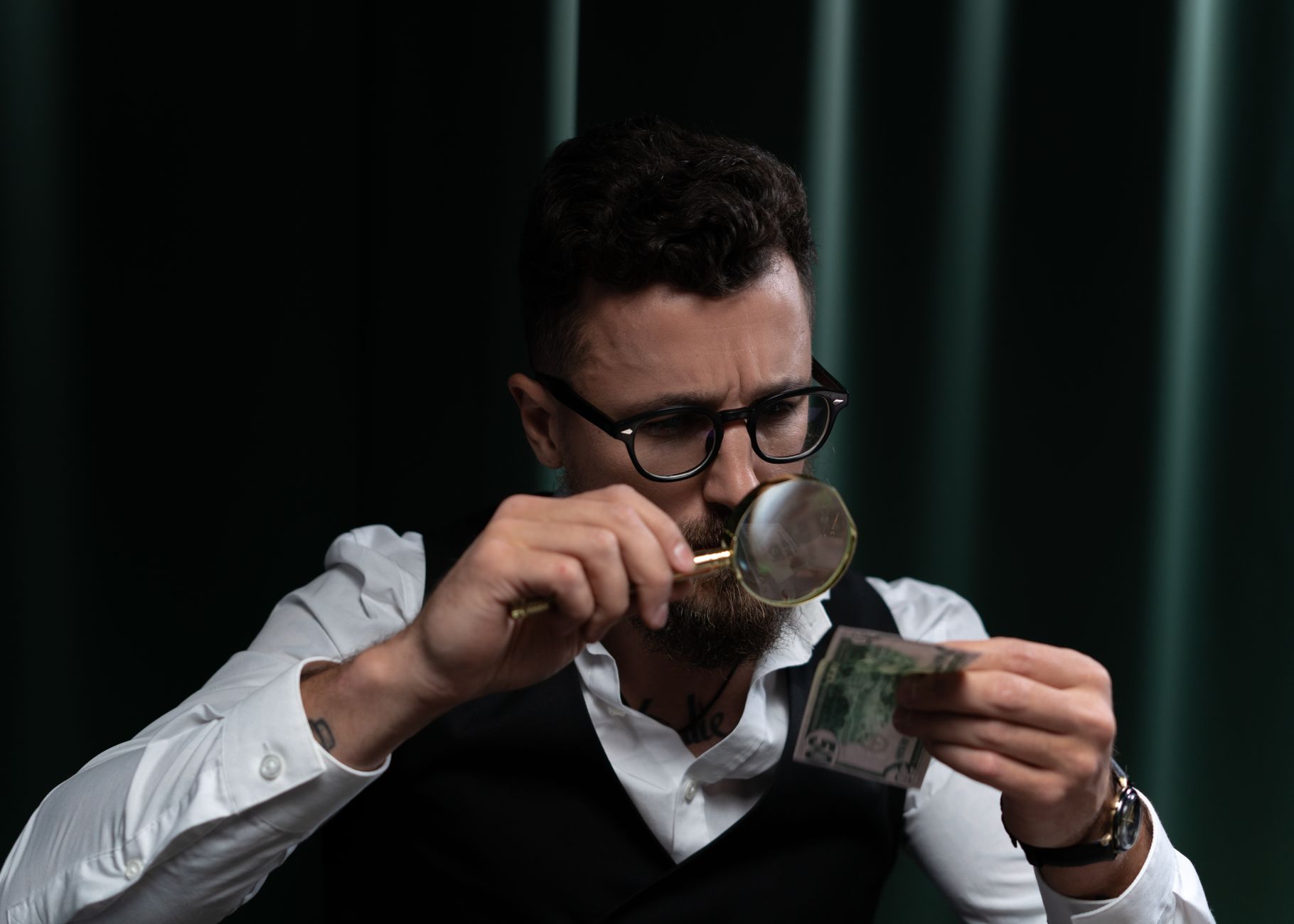 Focused adult inspecting a banknote closely with a magnifying glass indoors.