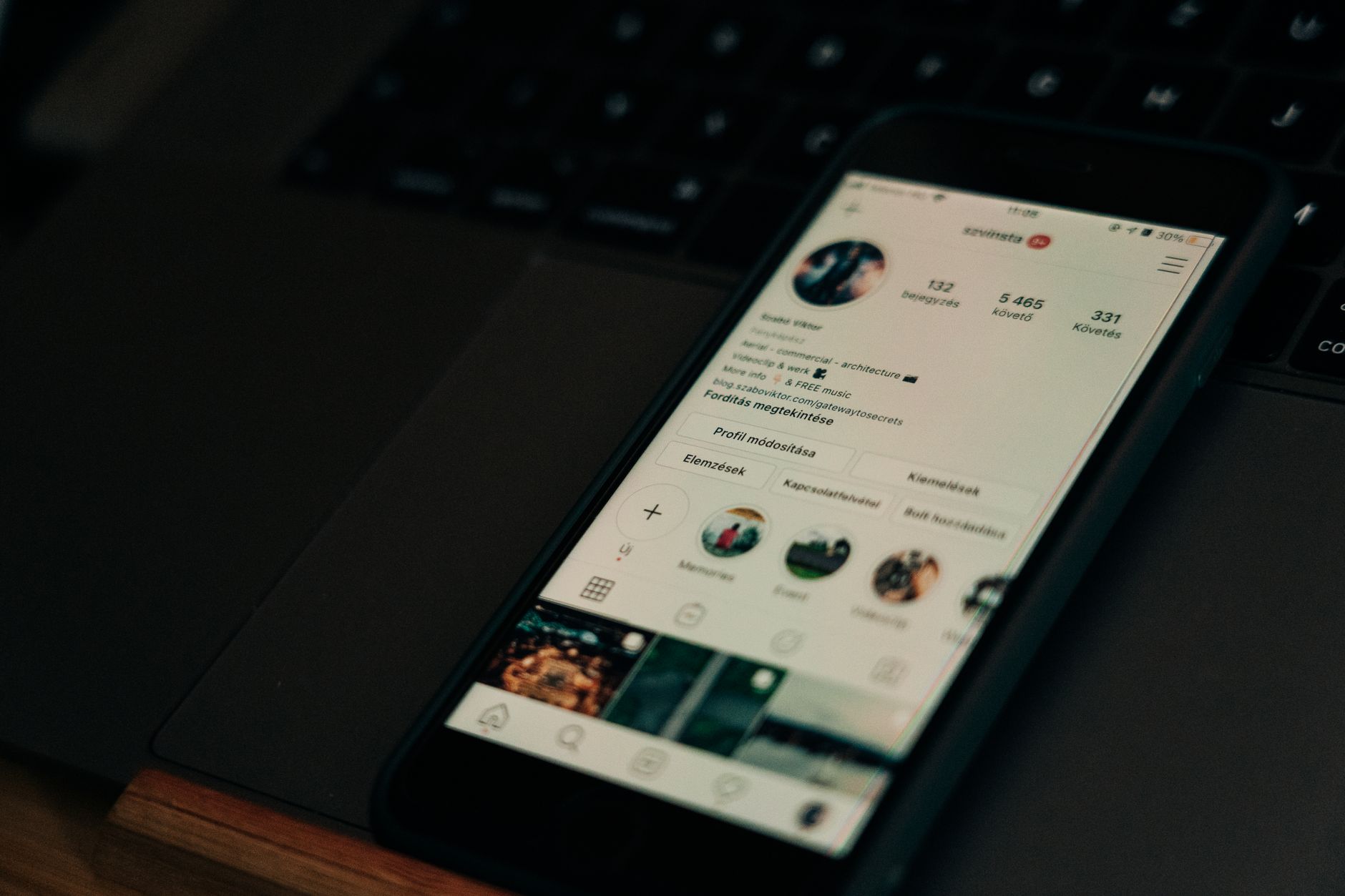 Smartphone displaying an Instagram profile with follower and post counts, resting on a laptop keyboard