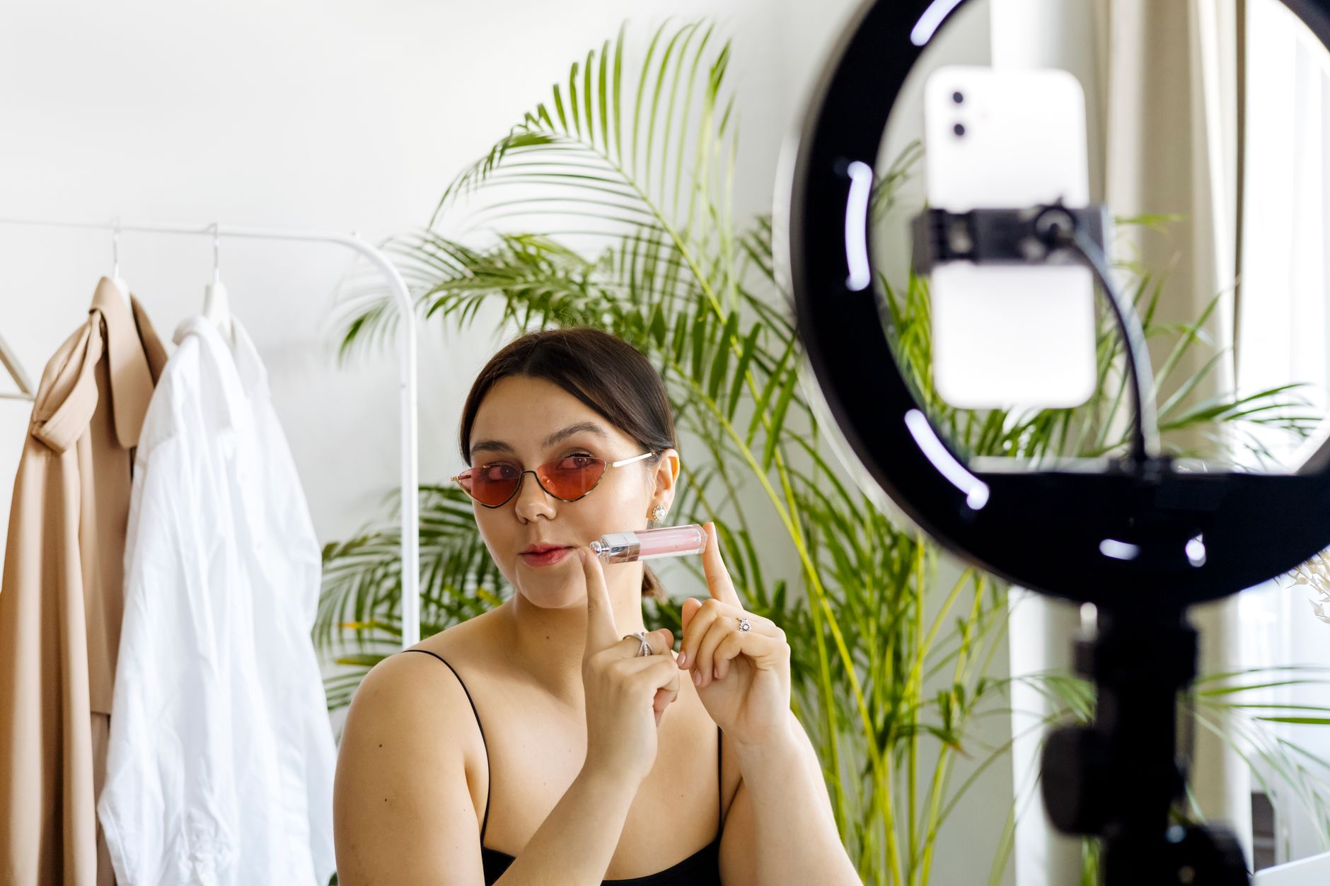 Woman holding a cosmetic product while filming herself with a smartphone and ring light