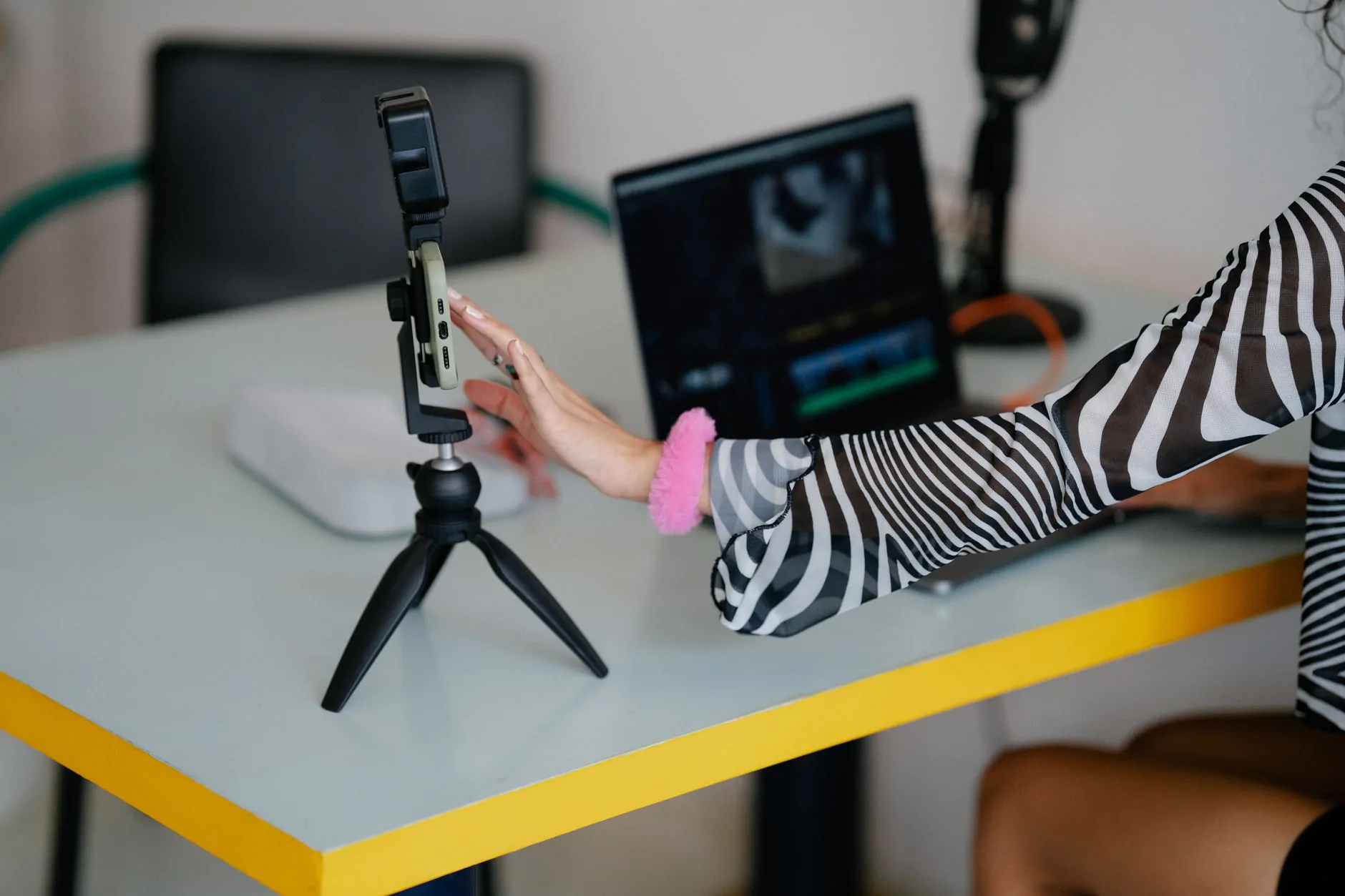 Creator adjusting a smartphone mounted on a tripod next to a laptop while filming content