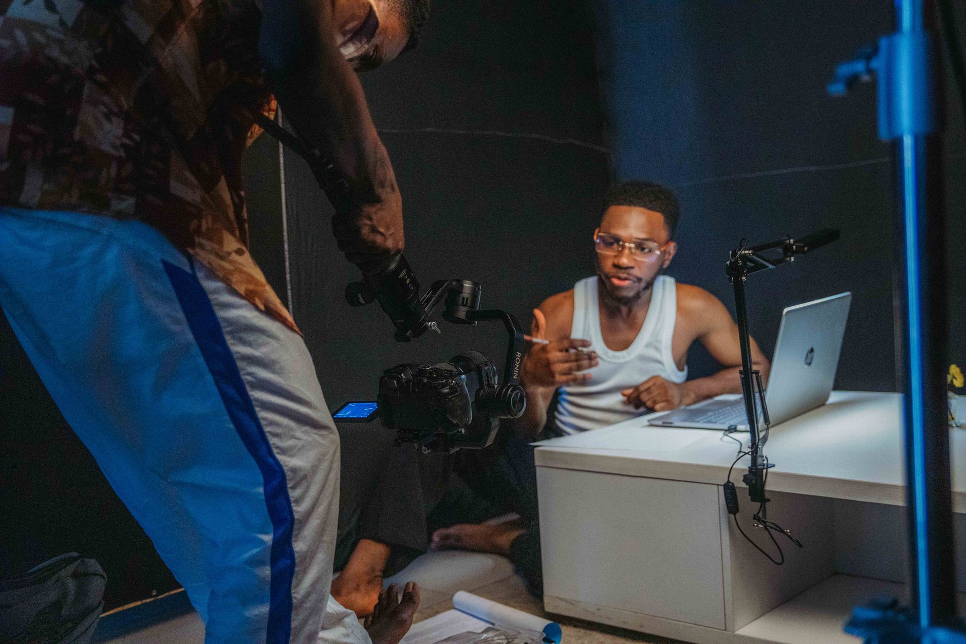 Two creators filming a video together at a desk with a laptop and a camera rig in a home studio.