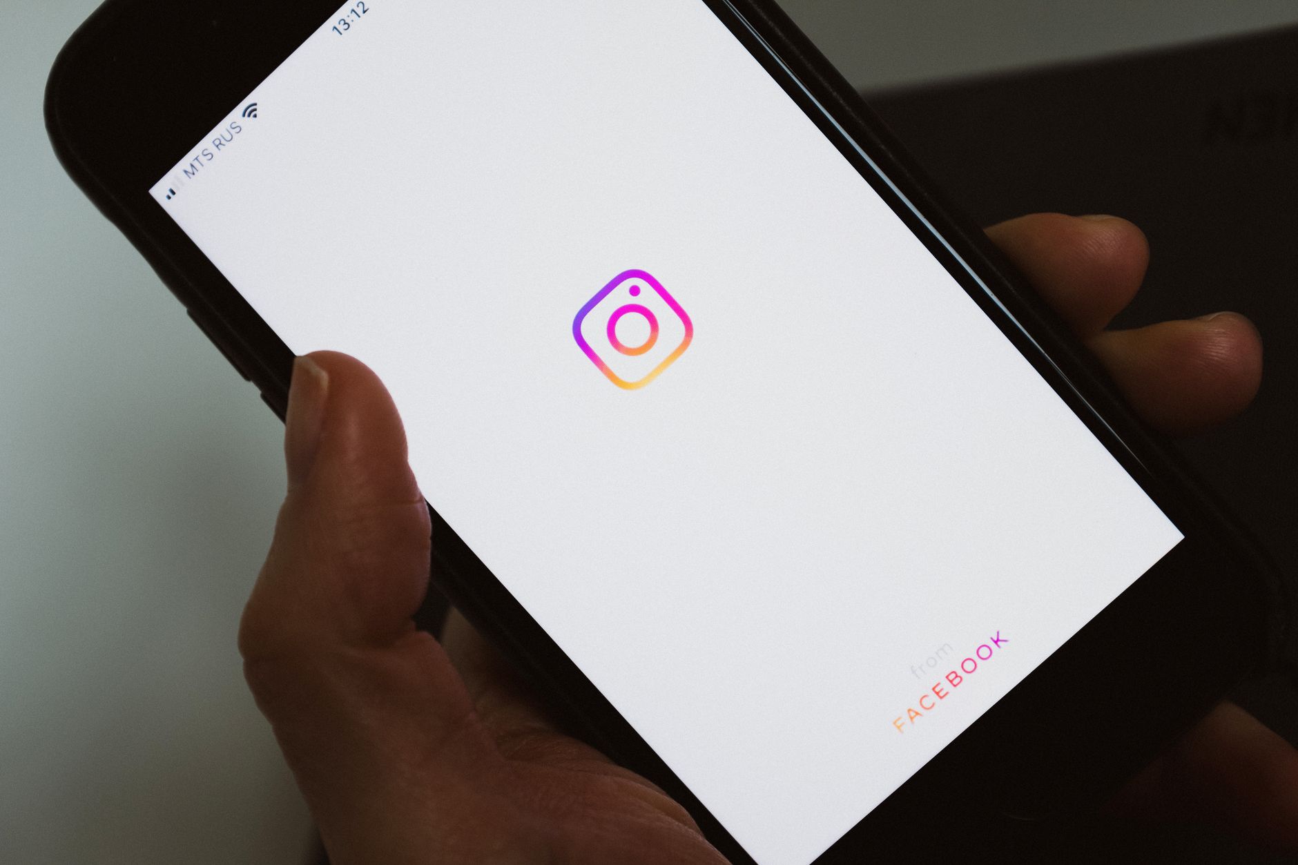 A hand holding a smartphone displaying the Instagram app logo on its loading screen.