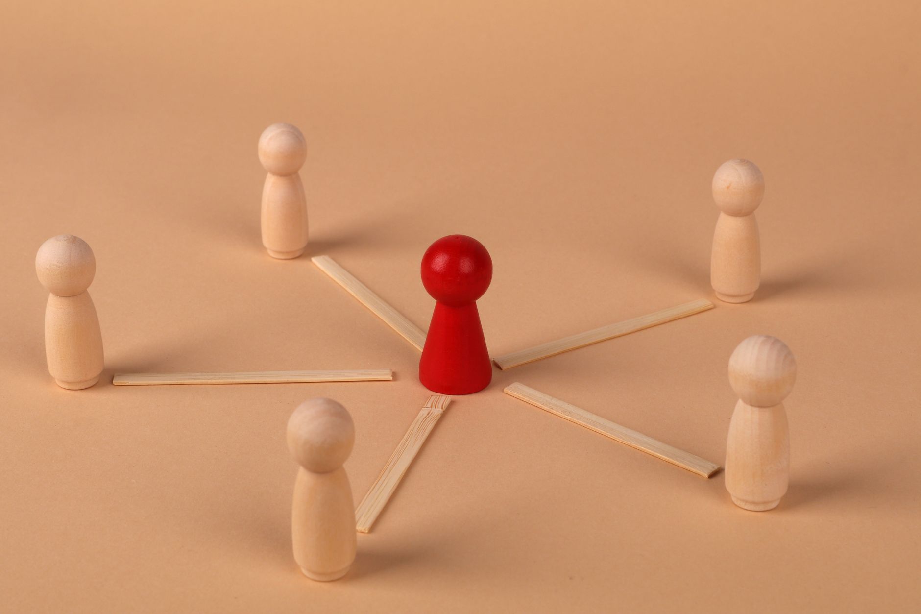 Red wooden figure connected by sticks to five light wooden figures standing around it