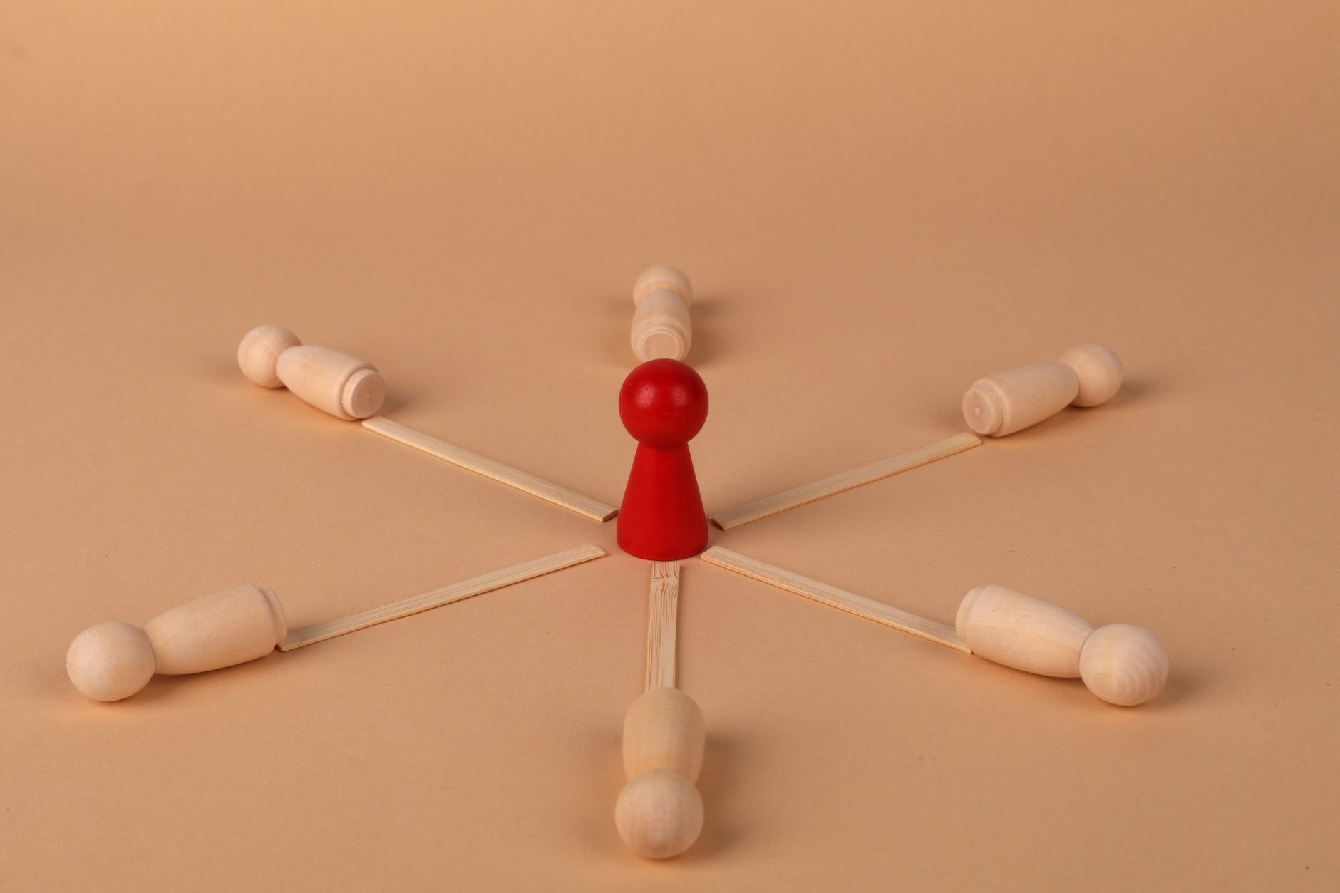 Red wooden figure connected by spokes to several wooden peg figures, representing one creator at the center of a coordinated team.