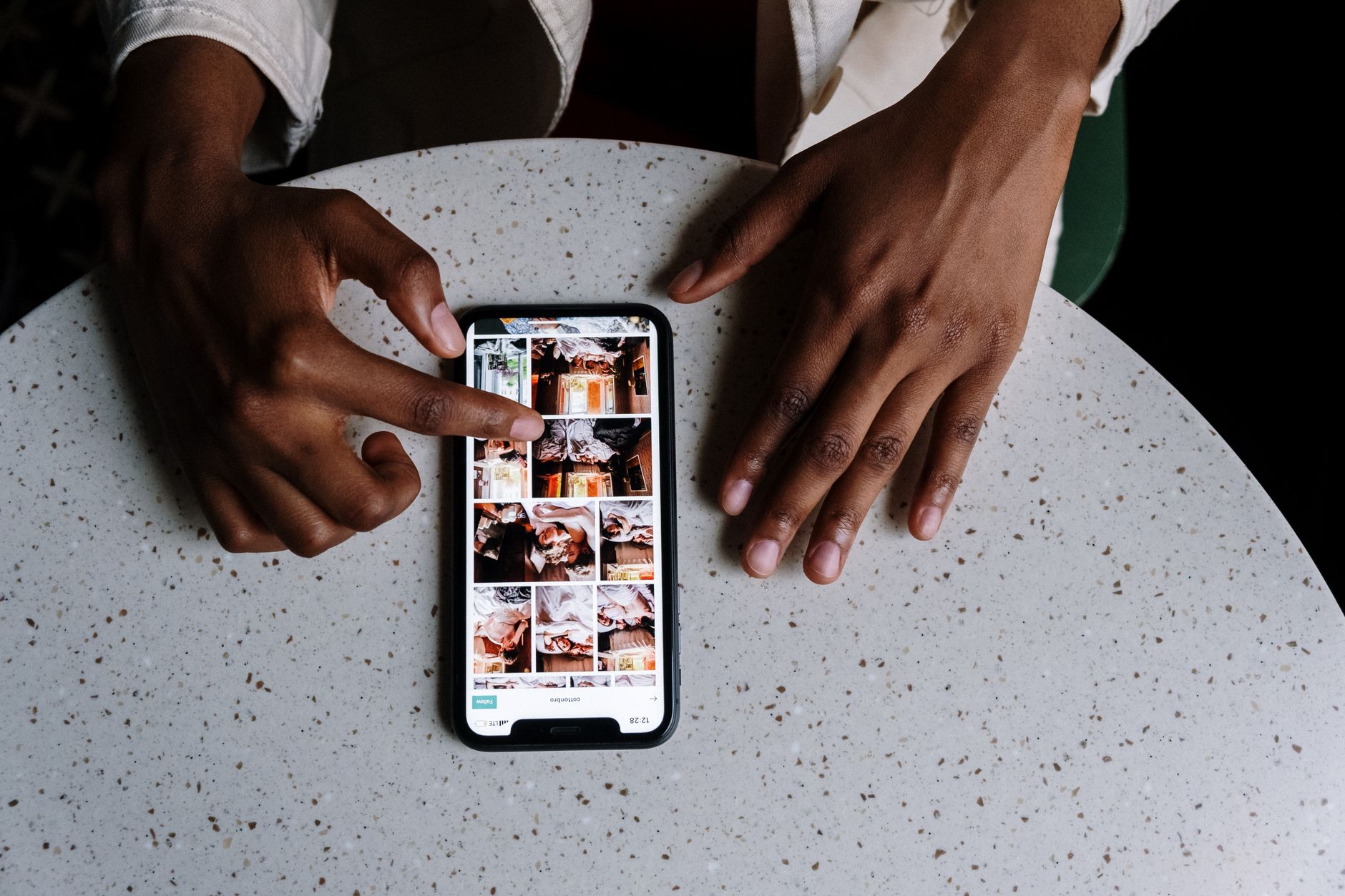 Hands interacting with a smartphone showing an Instagram-style photo grid on a cafe table