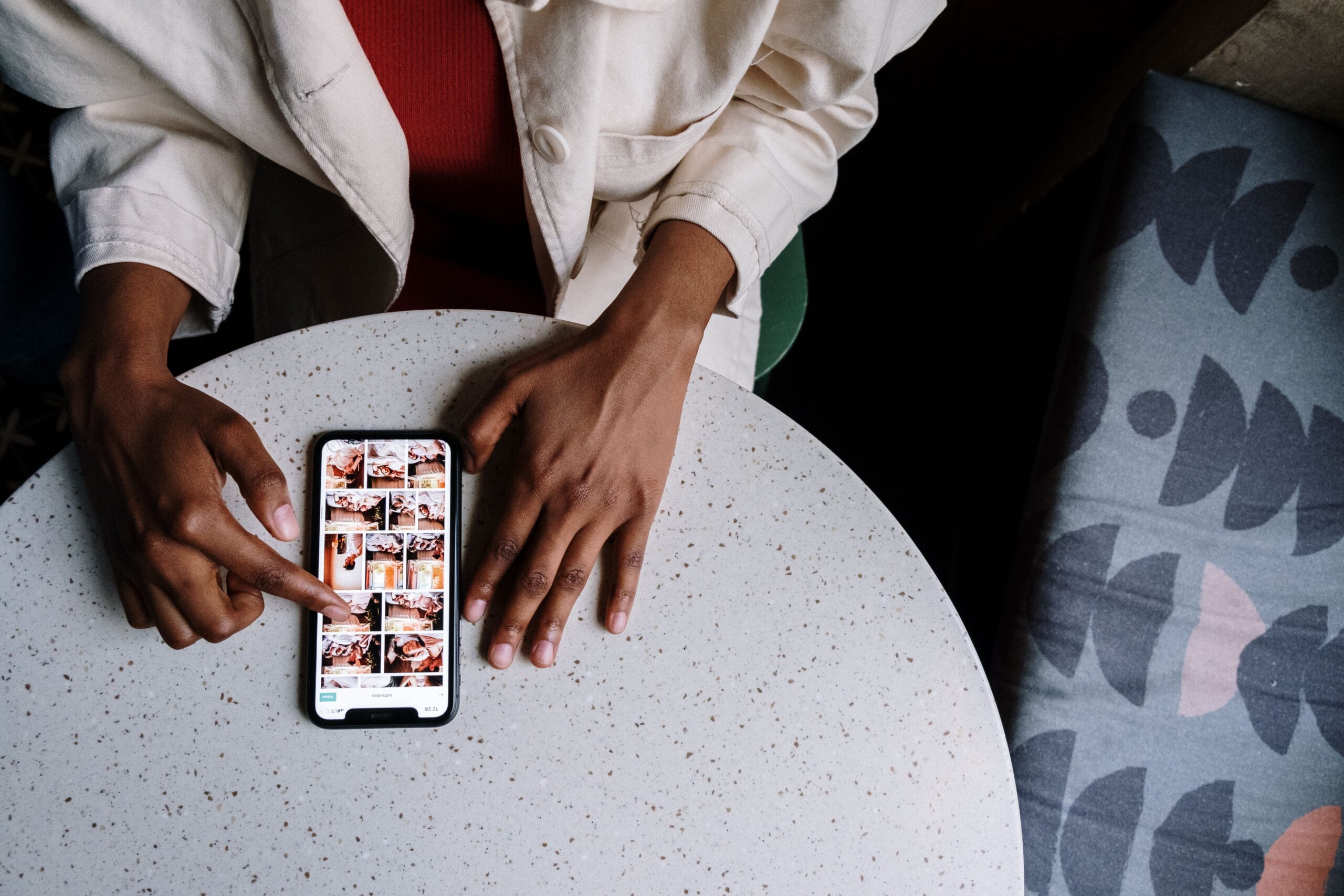 A person scrolling through a grid of personal photos on a smartphone at a cafe table