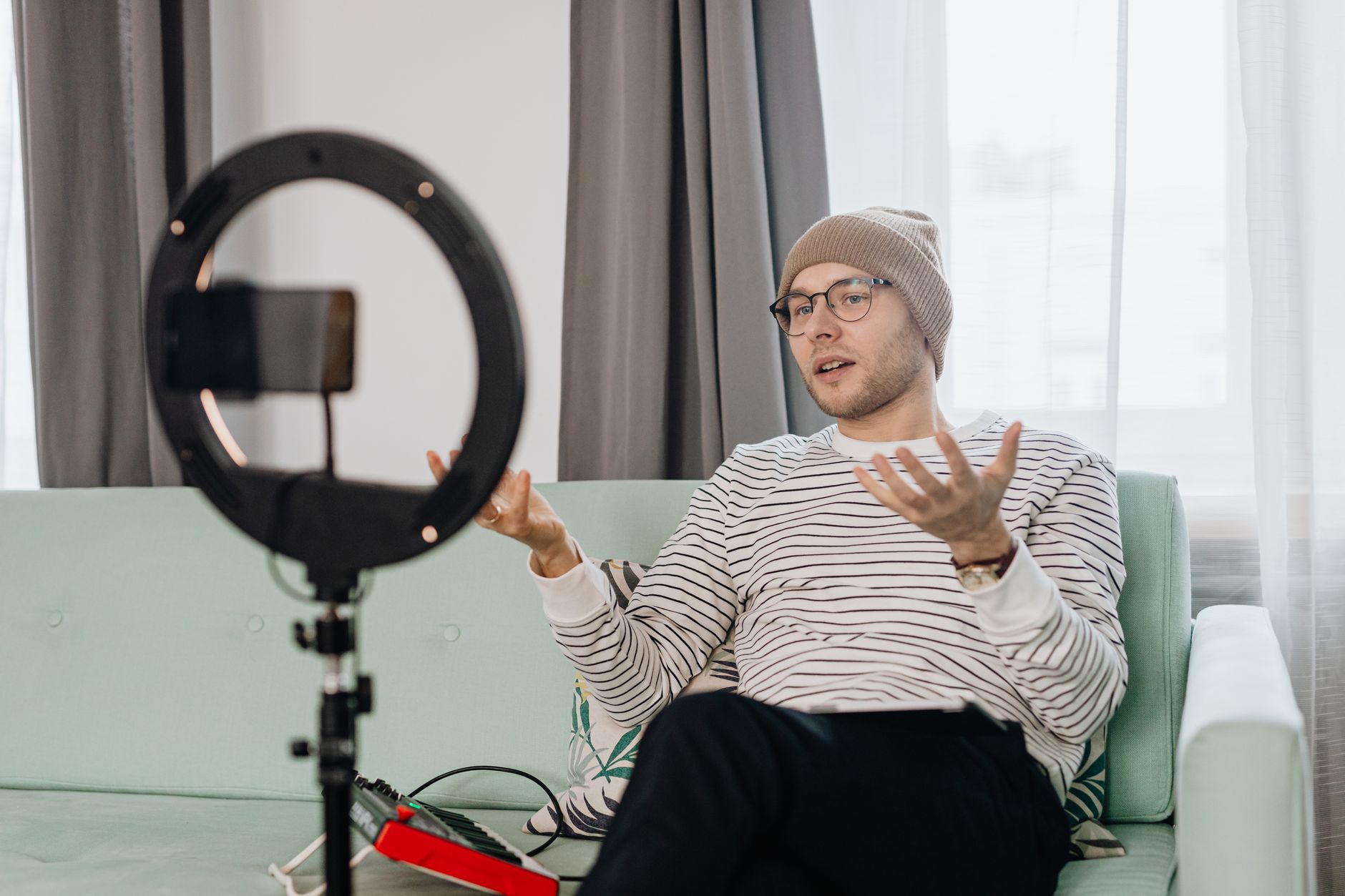 A man in a beanie using a ring light to vlog indoors on a couch