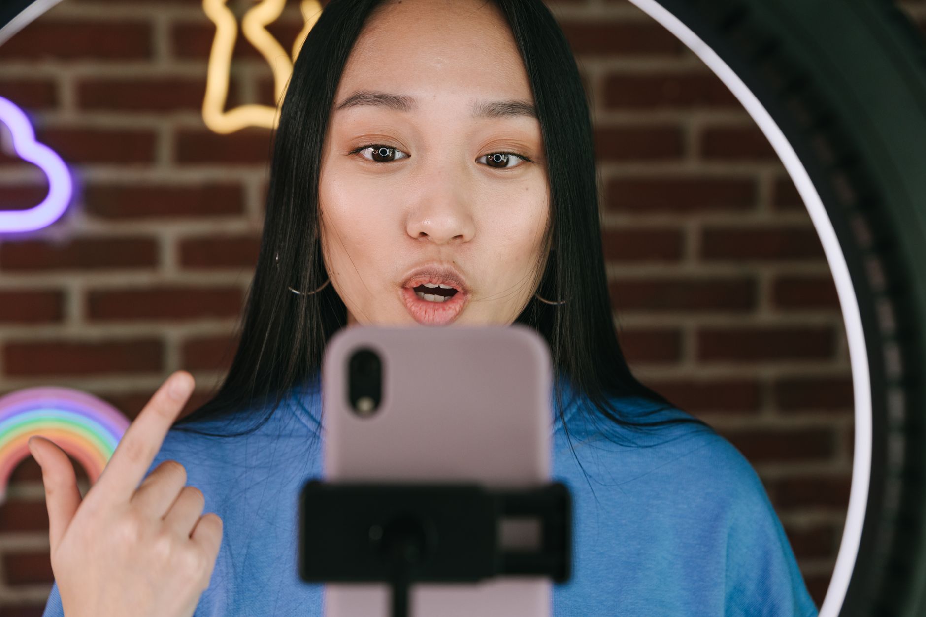 Woman recording herself talking on a smartphone with a ring light, creating content as a social media influencer.