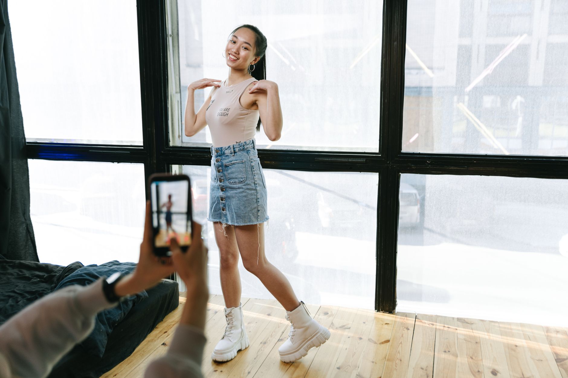 A young woman dancing while being recorded on a smartphone in a sunlit studio.