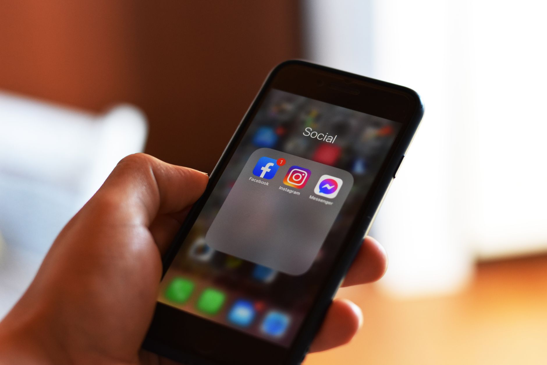 A hand holds a smartphone with a Social folder open showing the Instagram, Facebook and Messenger apps.