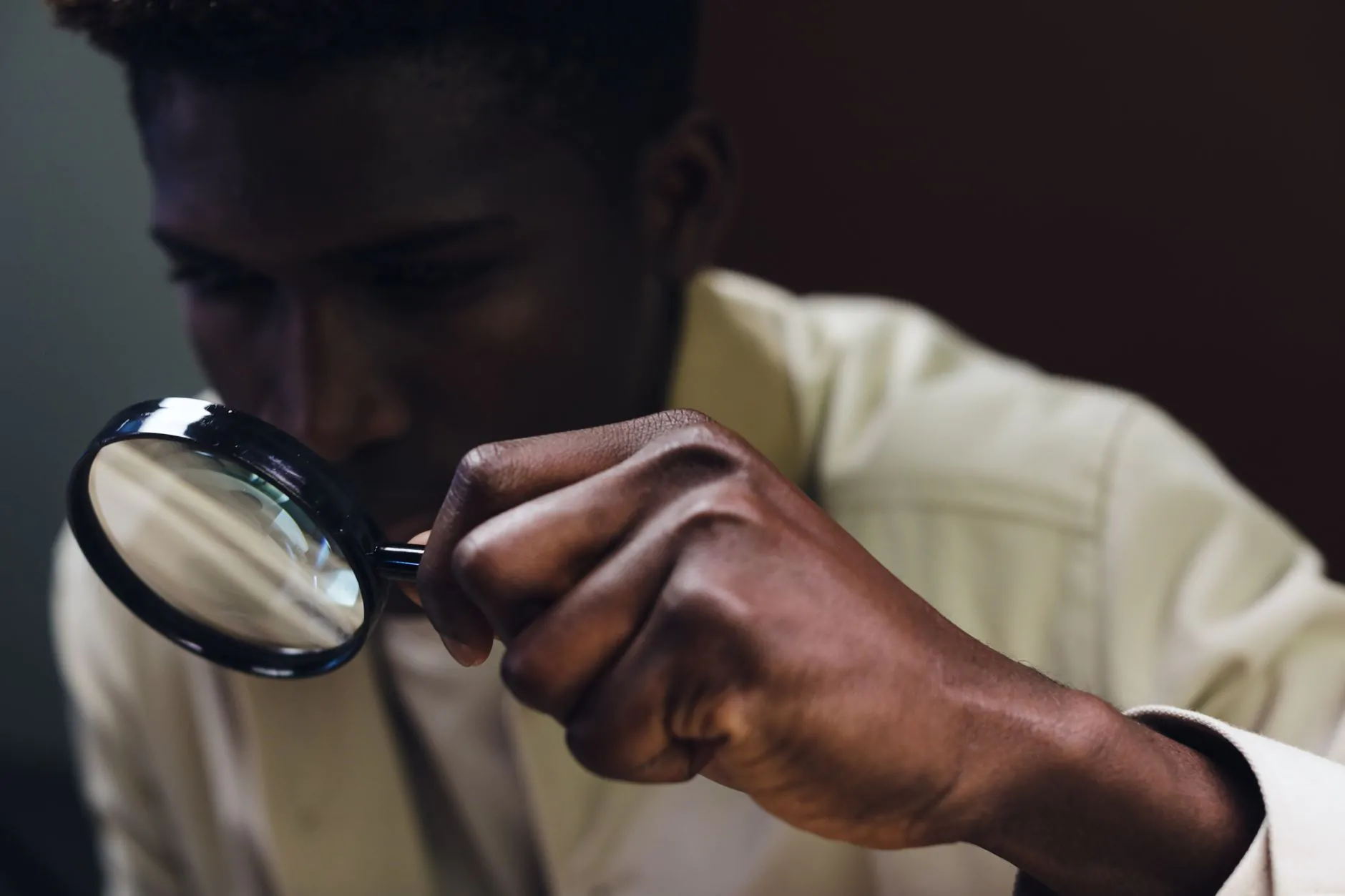A man closely examines an object with a magnifying glass, representing careful scrutiny and verification.